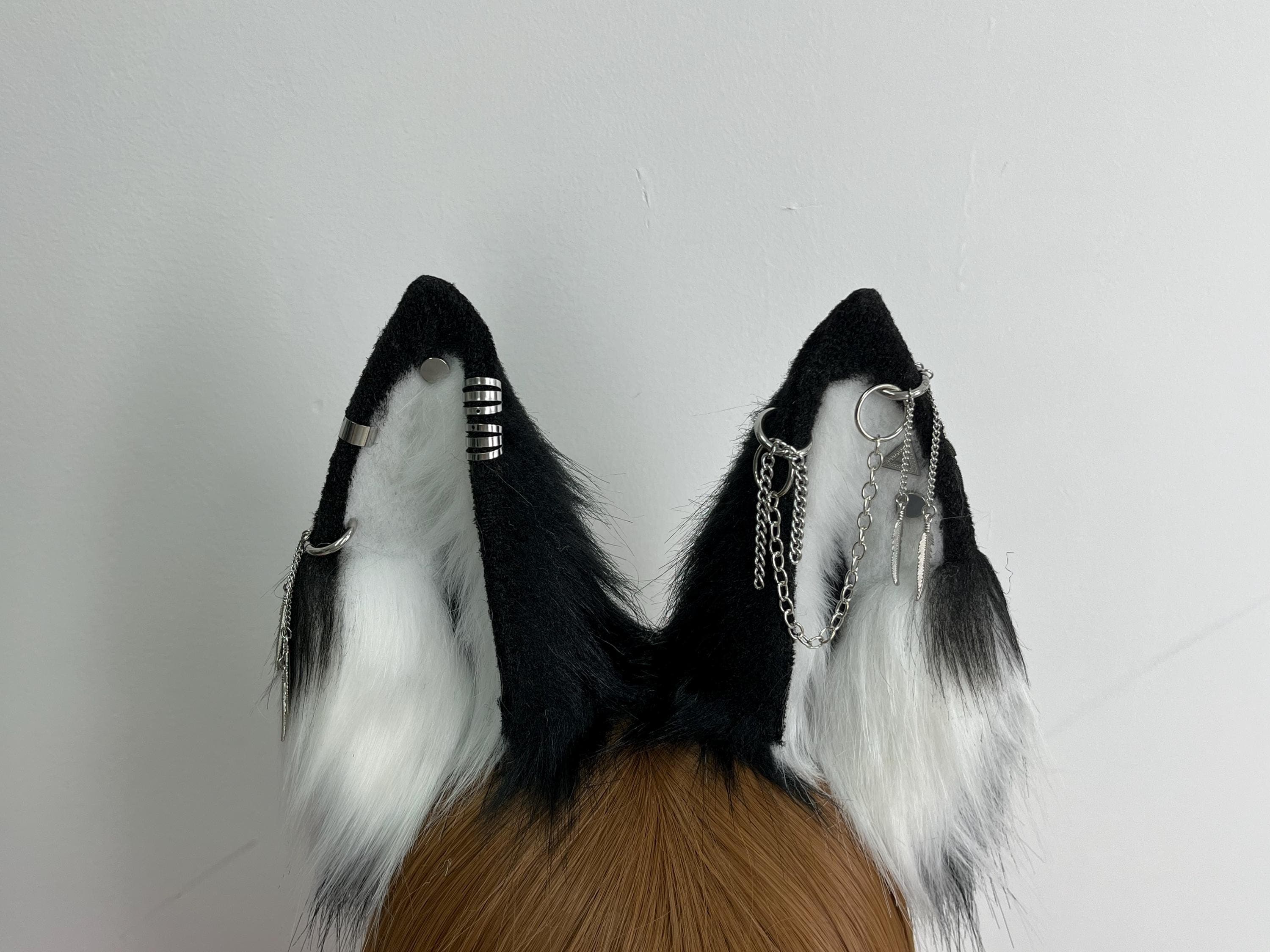 Back detail close up of black white wolf ears showing how silver chain piercings bar cuffs and feather charms attach to solid black outer ear construction with white fluffy inner plush structure visible, realistic faux fur wolf ear anatomy for therian alt fashion gothic punk cosplay. Perfect for furry convention kemonomimi Halloween anime character roleplay. Handmade plush ears with unique decorative metal accents rave festival streetwear photoshoot prop cosplayer gift.
