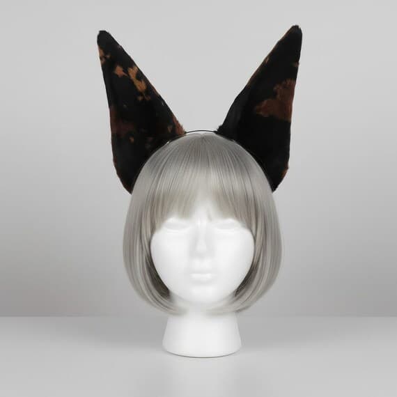 Dark brown spotted dog ear headband on mannequin head with silver grey wig. Tall pointed plush ears with dark tortoiseshell brown and black spotted pattern on slim metal headband. Realistic wild dog ears cosplay accessory for halloween anime con therian kemonomimi.
